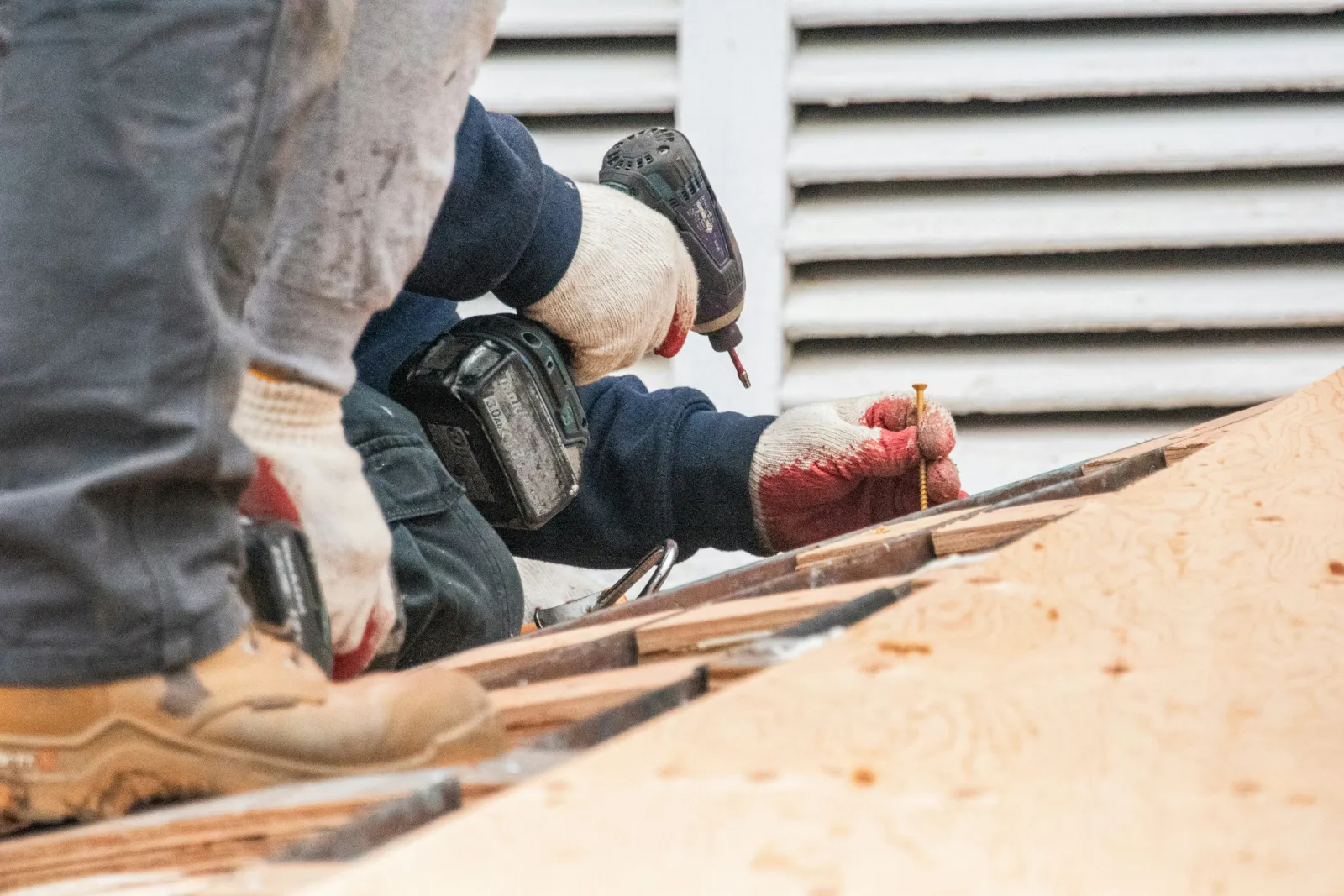 Gloved hands driving screws into a roof deck with a cordless drill.